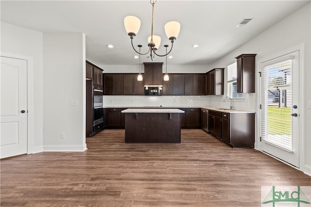 kitchen featuring stainless steel microwave, dark brown cabinets, a kitchen island, and a sink