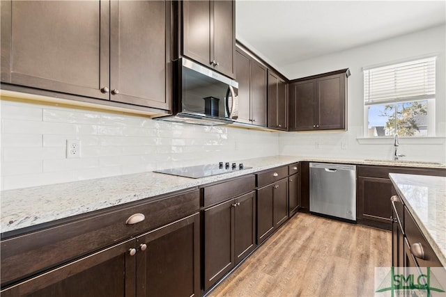 kitchen with a sink, stainless steel appliances, dark brown cabinets, light wood-type flooring, and backsplash