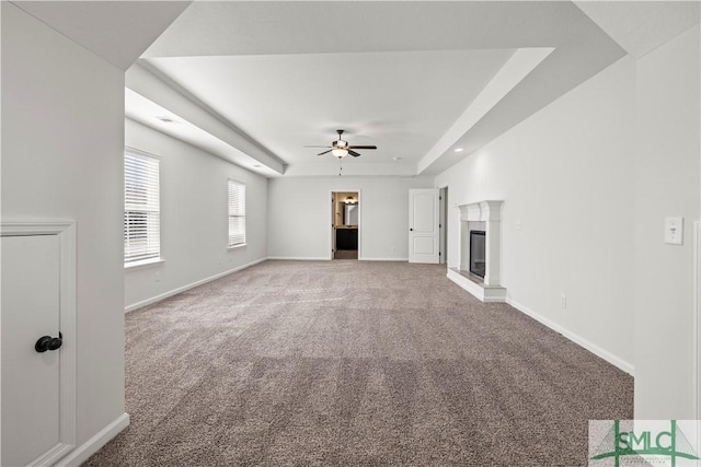 unfurnished living room with baseboards, a raised ceiling, carpet floors, and a glass covered fireplace