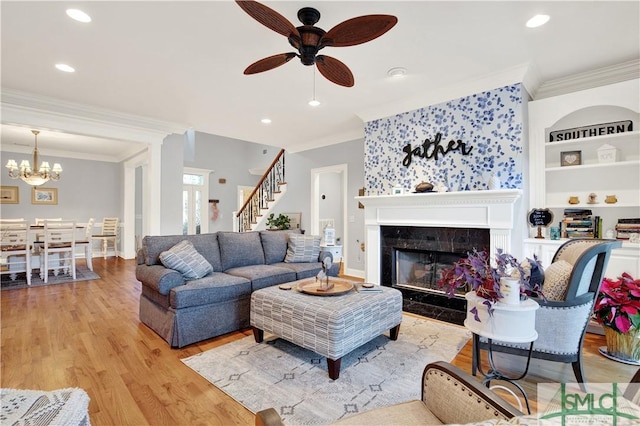 living room featuring light hardwood / wood-style floors, built in features, ceiling fan with notable chandelier, a premium fireplace, and crown molding