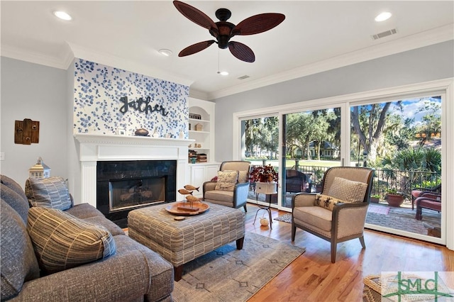 living room with crown molding, ceiling fan, light wood-type flooring, and built in features