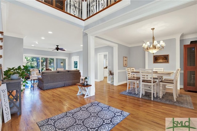 living room with ornamental molding, light wood-type flooring, and ceiling fan with notable chandelier