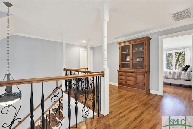 corridor with hardwood / wood-style floors, crown molding, and ornate columns