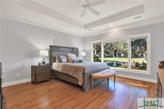 bedroom featuring wood-type flooring, ceiling fan, a tray ceiling, and crown molding