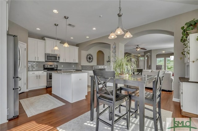 kitchen with hanging light fixtures, a kitchen island, white cabinets, appliances with stainless steel finishes, and ceiling fan