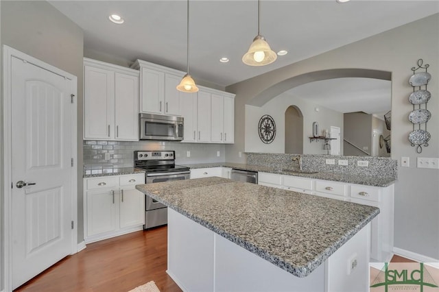 kitchen with stainless steel appliances, sink, white cabinetry, backsplash, and pendant lighting