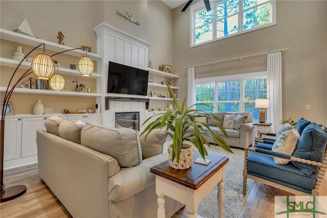 living area featuring a glass covered fireplace, plenty of natural light, light wood-style flooring, and a towering ceiling