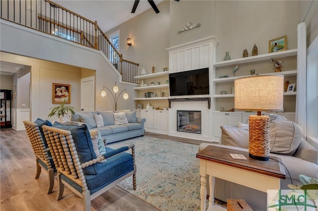 living area with a glass covered fireplace, built in features, a towering ceiling, and wood finished floors