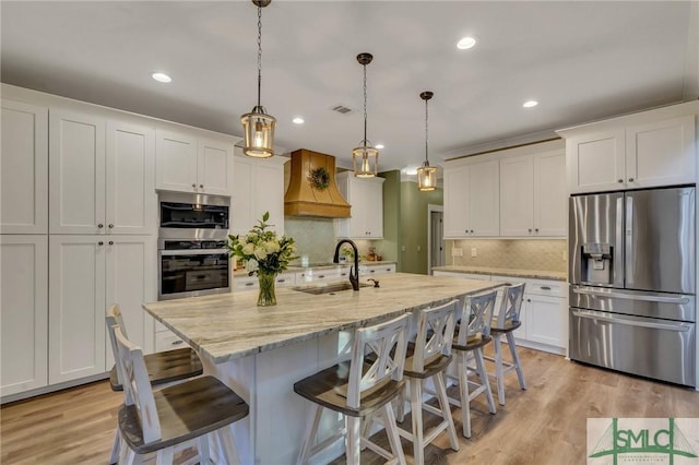 kitchen featuring light wood-style flooring, custom range hood, a sink, white cabinetry, and stainless steel appliances