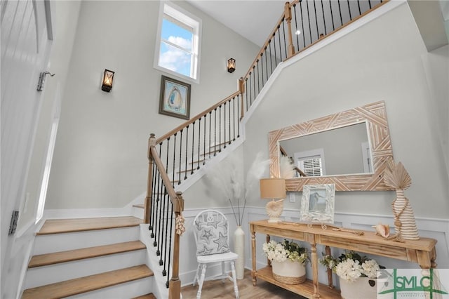 stairway with a decorative wall, wainscoting, a towering ceiling, and wood finished floors