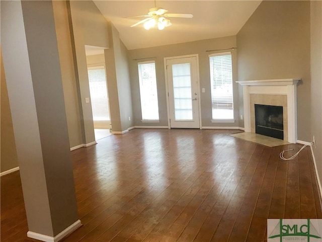 unfurnished living room featuring ceiling fan, dark hardwood / wood-style flooring, a tile fireplace, and vaulted ceiling