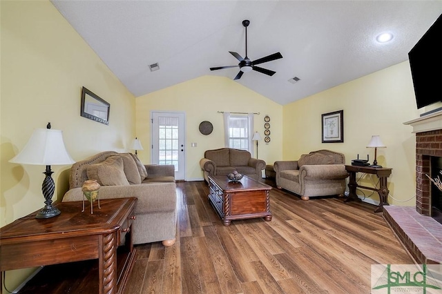 living room with ceiling fan, a brick fireplace, vaulted ceiling, and dark hardwood / wood-style floors