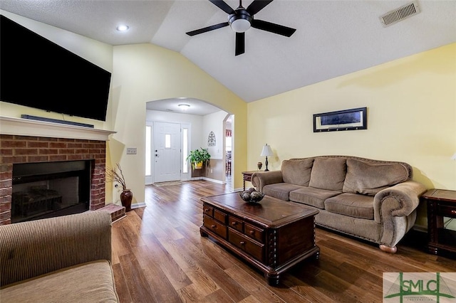 living room with a brick fireplace, ceiling fan, vaulted ceiling, and dark hardwood / wood-style floors