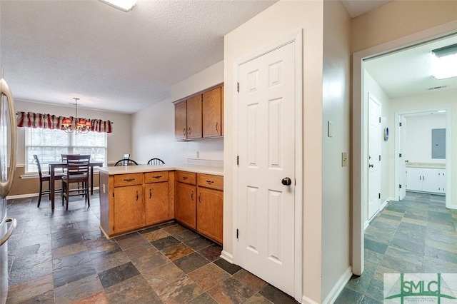 kitchen with a textured ceiling, hanging light fixtures, an inviting chandelier, and kitchen peninsula