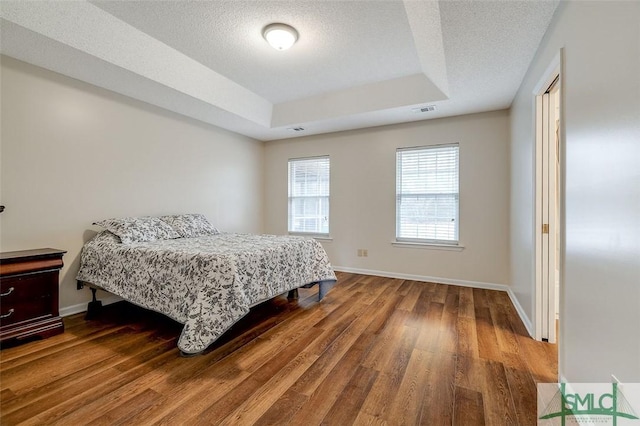 bedroom featuring hardwood / wood-style flooring, a textured ceiling, and a tray ceiling