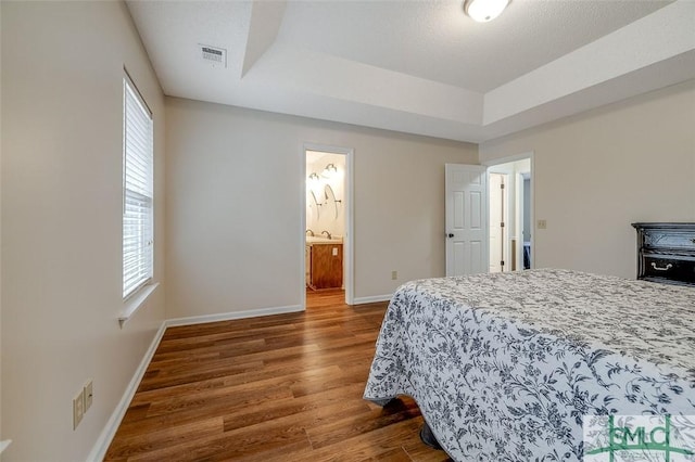 bedroom with dark wood-type flooring, connected bathroom, multiple windows, and a tray ceiling