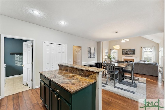 kitchen with hardwood / wood-style flooring, hanging light fixtures, a textured ceiling, a kitchen island, and light stone counters