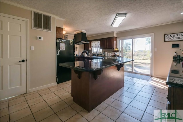 kitchen featuring a textured ceiling, black refrigerator, ventilation hood, ornamental molding, and a breakfast bar