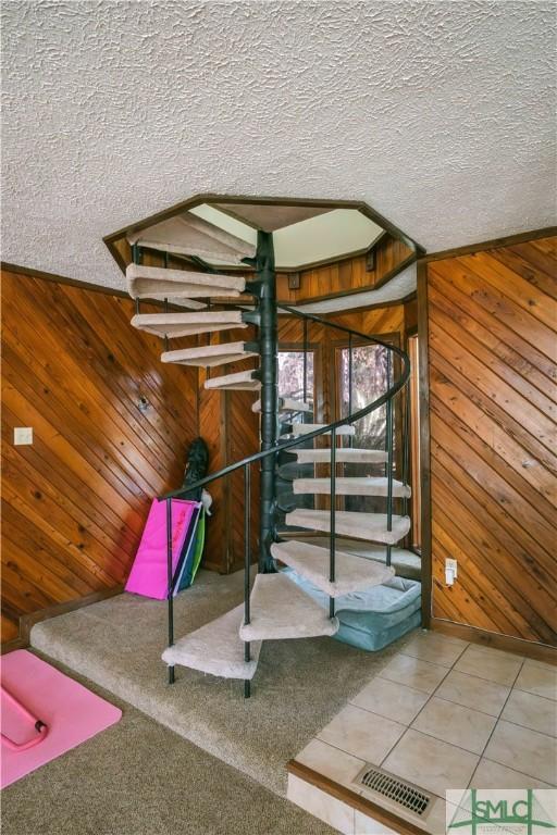 stairs with tile patterned floors, wood walls, and a textured ceiling