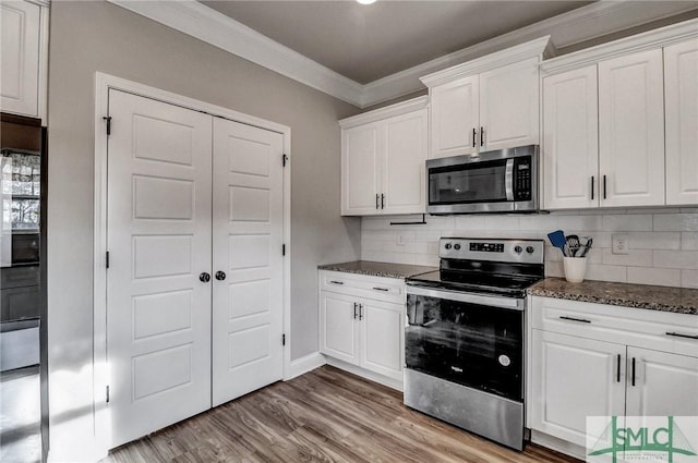 kitchen with appliances with stainless steel finishes, light hardwood / wood-style flooring, white cabinets, decorative backsplash, and crown molding