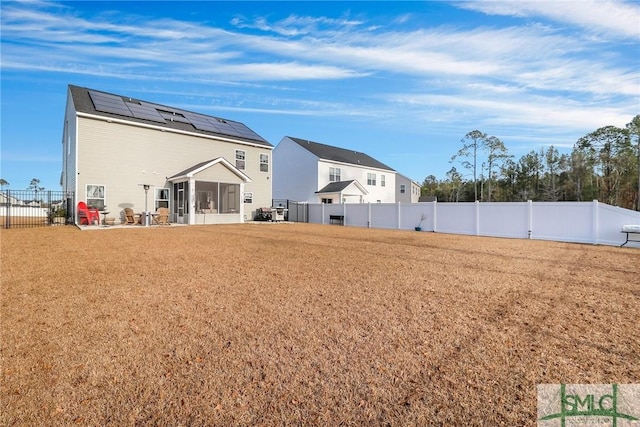 back of property with a sunroom, a lawn, and solar panels