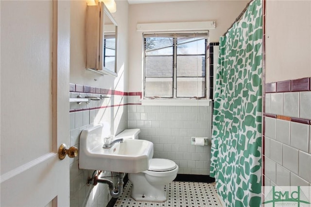 bathroom with toilet, a shower with curtain, tile walls, and sink