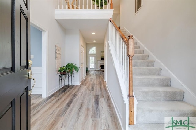 foyer entrance featuring a high ceiling, a fireplace, visible vents, stairs, and light wood-type flooring