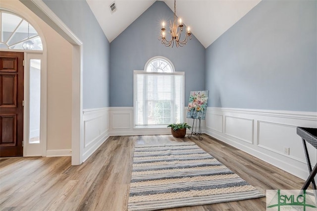 foyer entrance with visible vents, wainscoting, wood finished floors, vaulted ceiling, and a notable chandelier