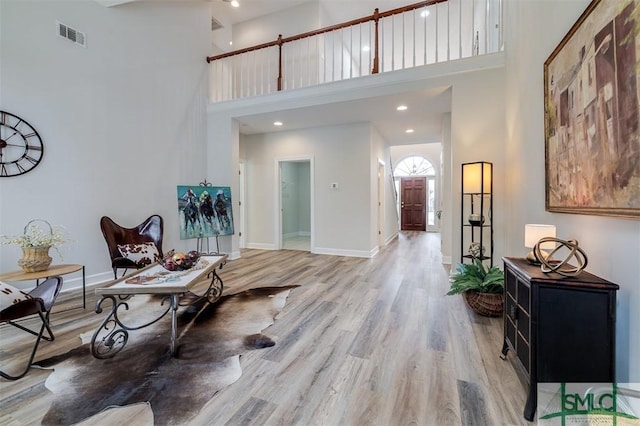 interior space featuring light wood-type flooring, visible vents, a high ceiling, and baseboards