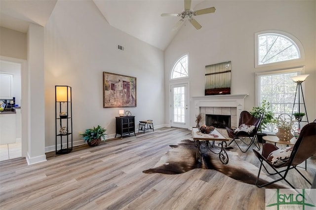 living room with high vaulted ceiling, wood finished floors, visible vents, baseboards, and a tiled fireplace