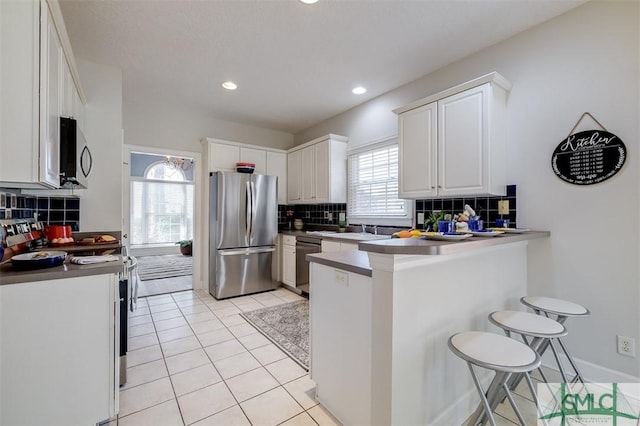 kitchen featuring stainless steel appliances, white cabinets, light tile patterned flooring, a peninsula, and a kitchen breakfast bar