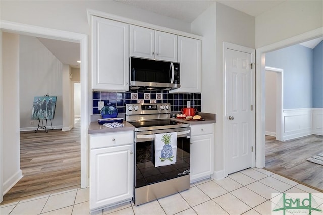 kitchen with stainless steel appliances, white cabinets, backsplash, and light tile patterned floors