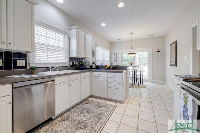 kitchen featuring light tile patterned floors, dishwasher, dark countertops, a peninsula, and white cabinetry