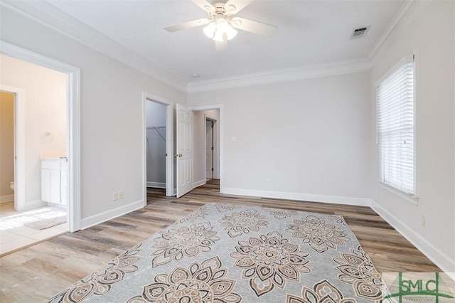 unfurnished bedroom with a walk in closet, crown molding, baseboards, and wood finished floors