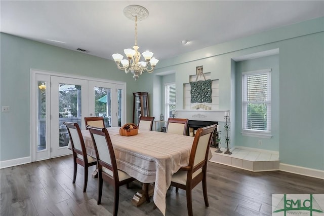 dining area with a healthy amount of sunlight, dark wood-type flooring, a tile fireplace, and a chandelier