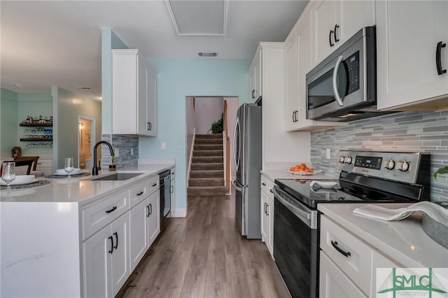 kitchen featuring appliances with stainless steel finishes, white cabinetry, light hardwood / wood-style floors, sink, and decorative backsplash