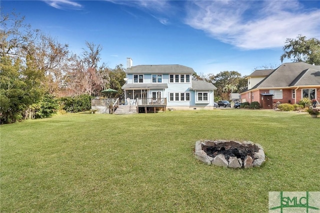 back of property with a lawn, an outdoor fire pit, a wooden deck, and a sunroom