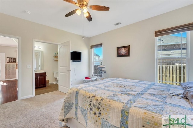 bedroom featuring ceiling fan, light carpet, visible vents, baseboards, and ensuite bath