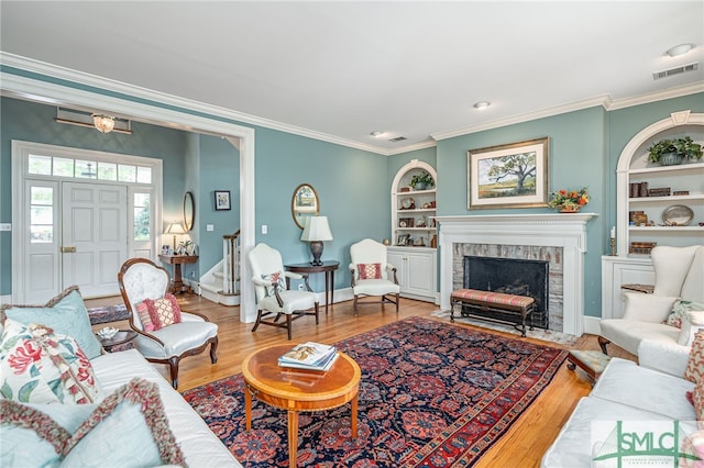 living room with hardwood / wood-style floors, built in features, crown molding, and a brick fireplace