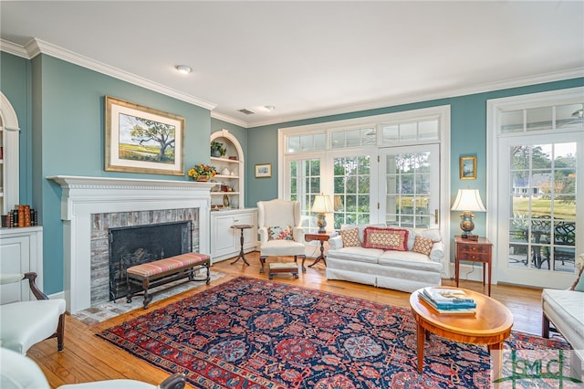 living room with a fireplace, crown molding, built in features, and wood-type flooring