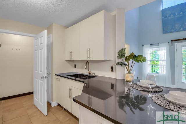 kitchen with light tile patterned floors, sink, white cabinetry, and a textured ceiling