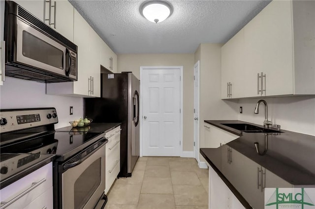 kitchen featuring sink, light tile patterned flooring, appliances with stainless steel finishes, a textured ceiling, and white cabinets