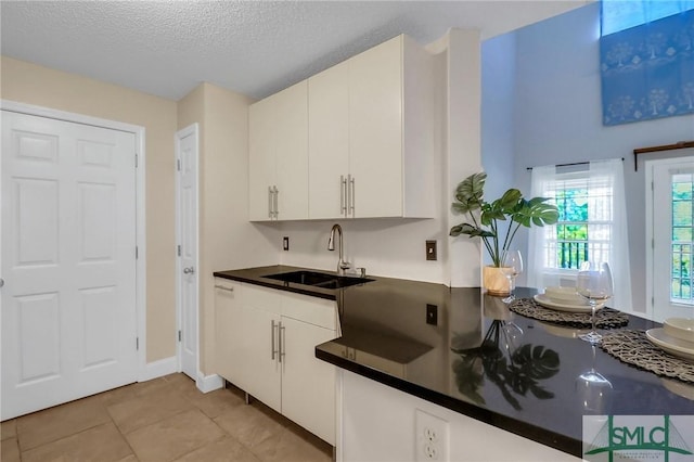 kitchen with light tile patterned floors, sink, white cabinetry, and a textured ceiling