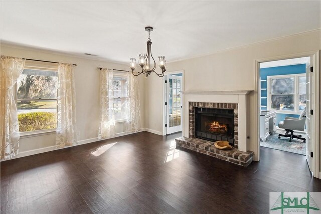 unfurnished living room featuring dark wood-type flooring, a notable chandelier, crown molding, and a brick fireplace