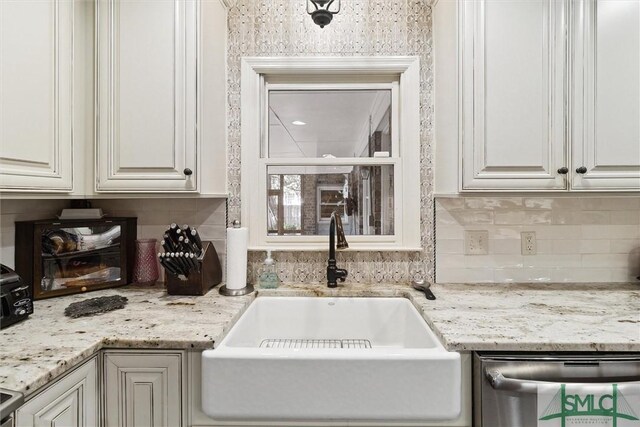 kitchen featuring stainless steel dishwasher, backsplash, sink, and white cabinetry