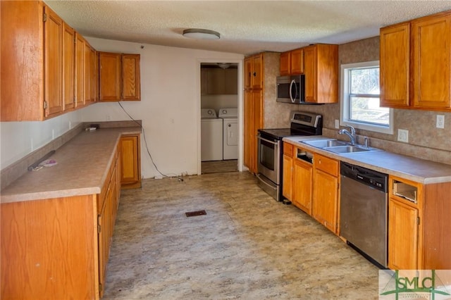 kitchen with a textured ceiling, stainless steel appliances, sink, and washer and dryer