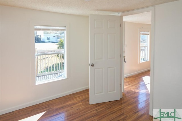 empty room with a textured ceiling, dark hardwood / wood-style floors, and plenty of natural light