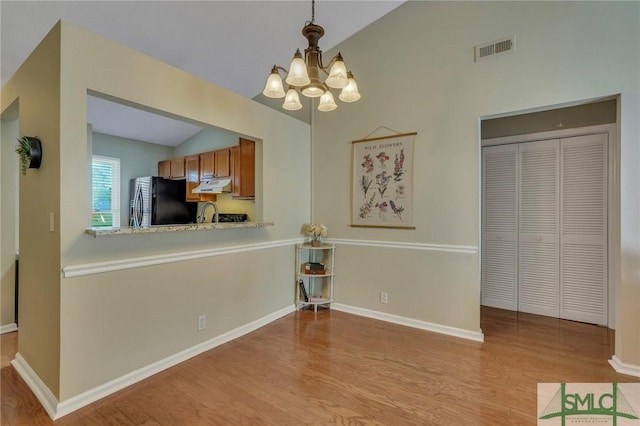 kitchen with lofted ceiling, decorative light fixtures, black refrigerator with ice dispenser, light hardwood / wood-style flooring, and a chandelier