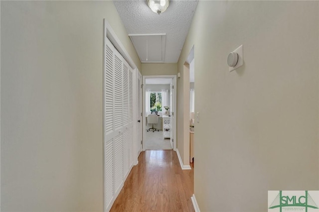 corridor with a textured ceiling and light wood-type flooring