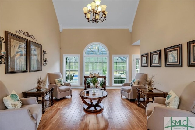 living room with light wood-type flooring, an inviting chandelier, ornamental molding, and a towering ceiling